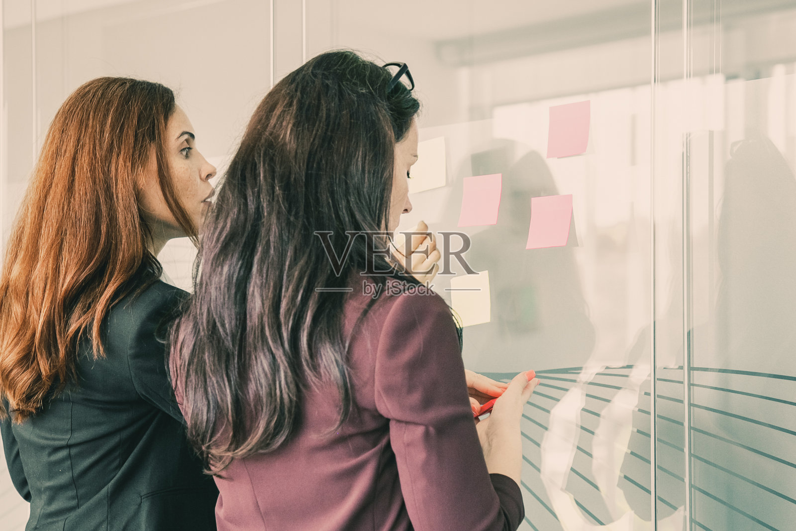 专注的女商人在玻璃墙上贴纸条照片摄影图片