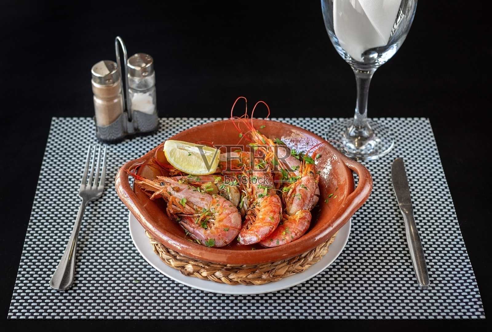 煮熟的虾在一个陶碗里，刀叉在旁边和一杯水。可食用的食物。照片摄影图片