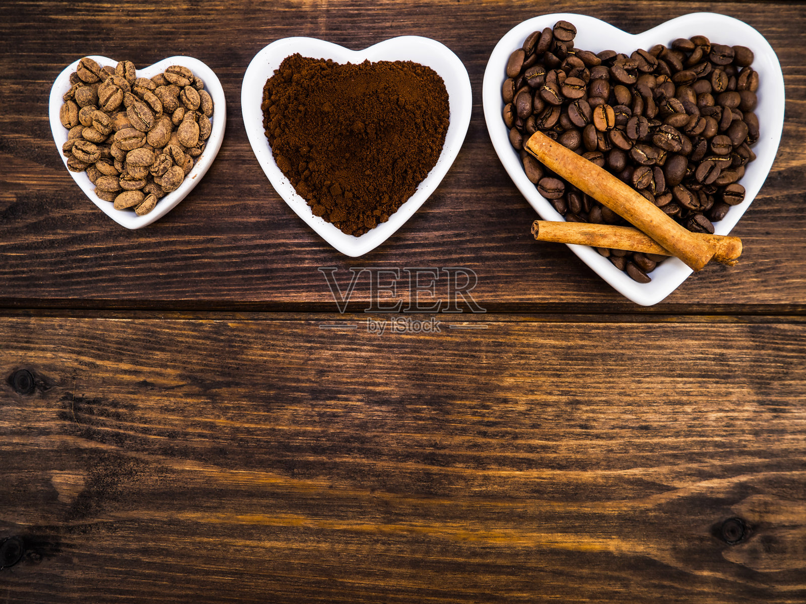 在一个白色的心形盘子里，木质的背景上放着咖啡豆和磨碎的粉末。背景和纹理。照片摄影图片