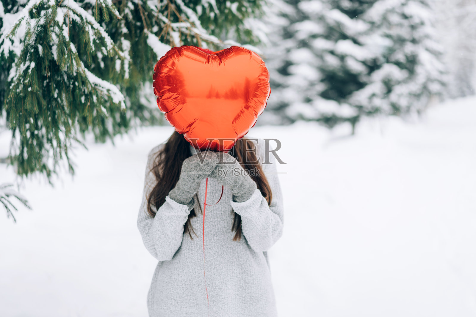 拿着红色心形气球的女人。以白雪覆盖的公园为背景的浪漫情调照片摄影图片