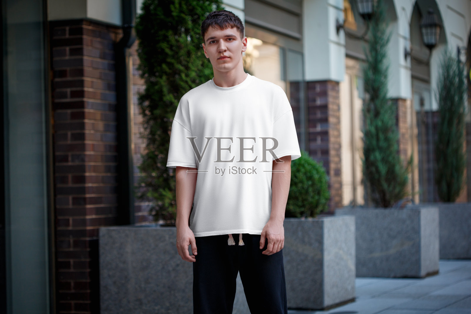 一个穿着深色裤子的家伙穿着白色t恤的模型，时髦的城市风格的衣服在模糊的街道背景上。照片摄影图片