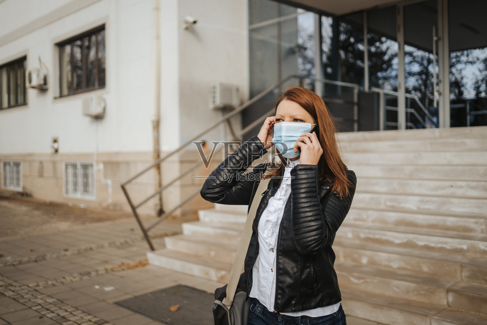 年轻的女商人戴着口罩，站在办公楼对面打电话照片摄影图片