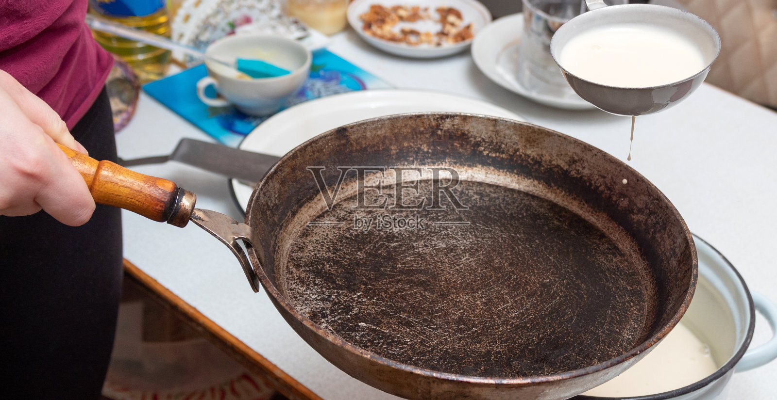 用勺子把做煎饼的面团收集起来，然后倒入煎锅里。马斯伦尼察庆典的准备工作。有选择性的重点。照片摄影图片