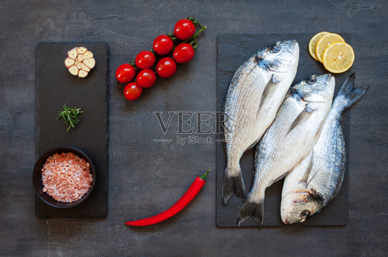 新鲜的剑鱼，加入香料，大蒜，柠檬和调味料，放在黑色砧板上。俯视图，复制空间。照片摄影图片