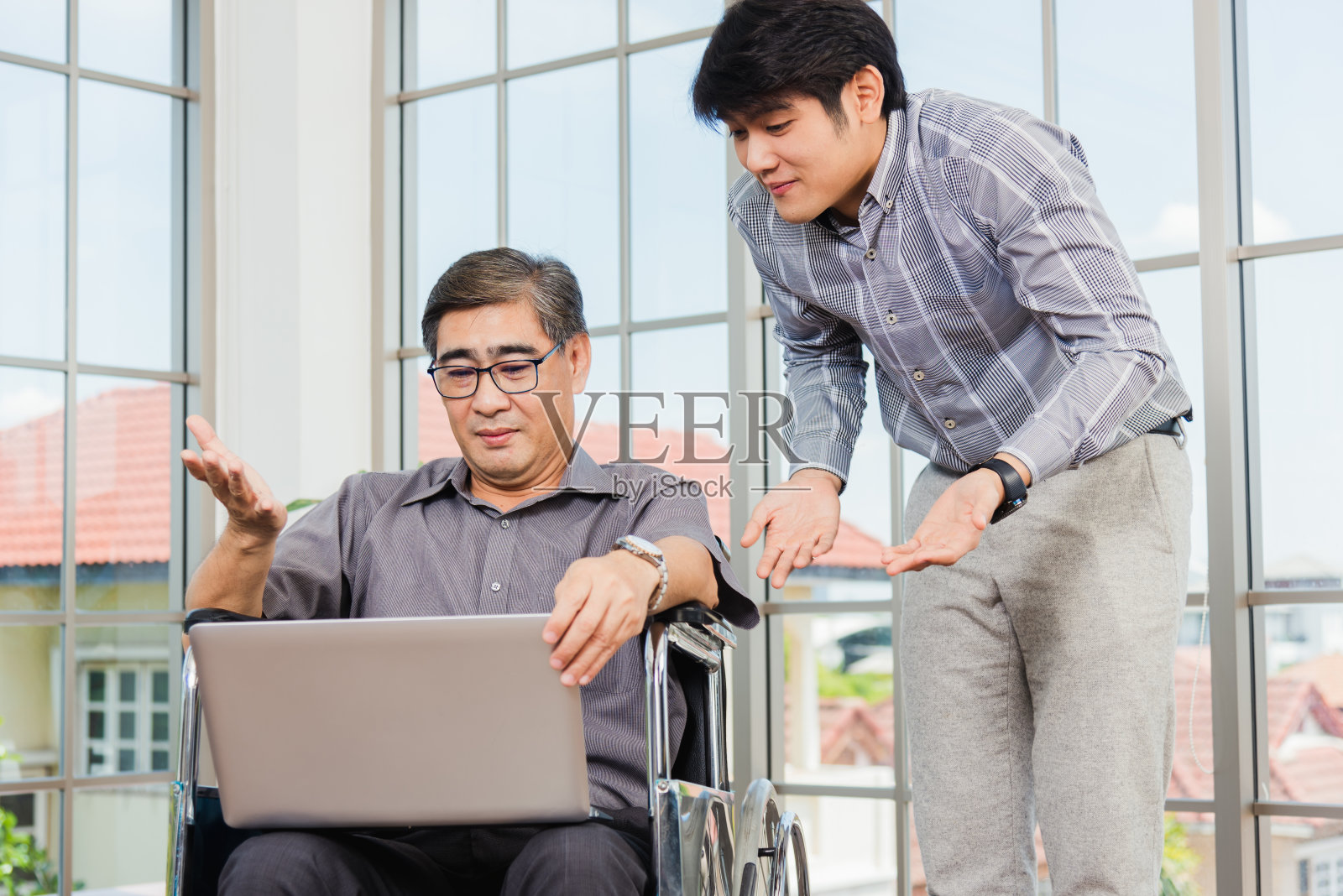 坐在轮椅上的父亲和他的儿子在用笔记本电脑进行视频电话会议照片摄影图片