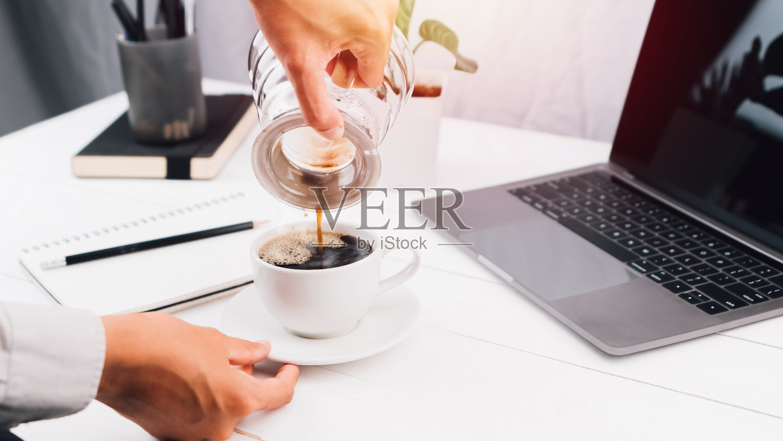选择性聚焦用手倒咖啡的器具放在杯子上办公。早上准备好开始艰苦的工作照片摄影图片
