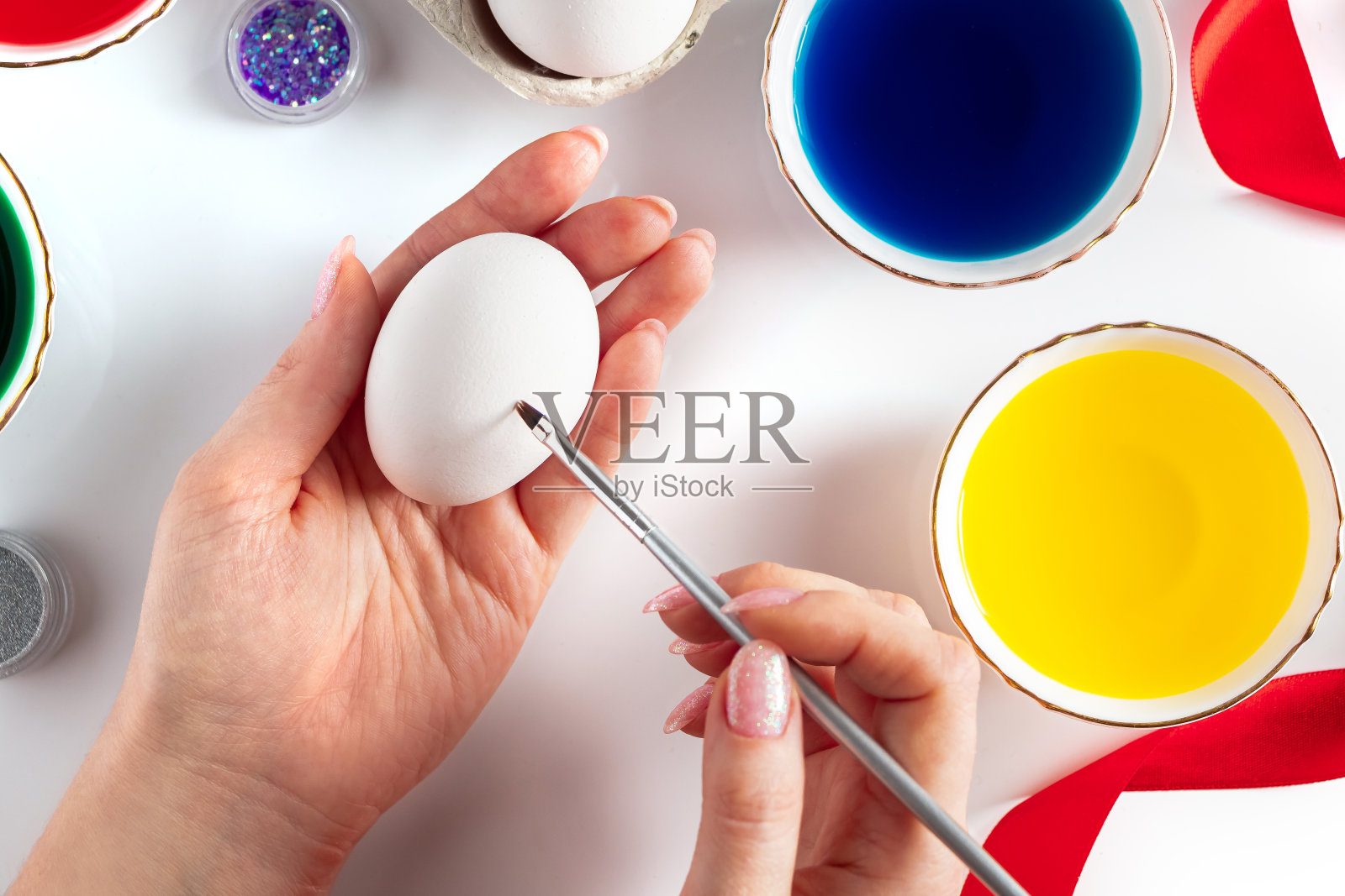 年轻女子用彩色颜料在复活节白色的蛋上作画。照片摄影图片