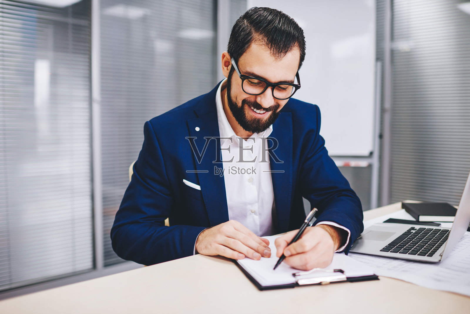 快乐的白人男经理戴着光学眼镜，在办公桌前用笔记本电脑撰写商业计划照片摄影图片