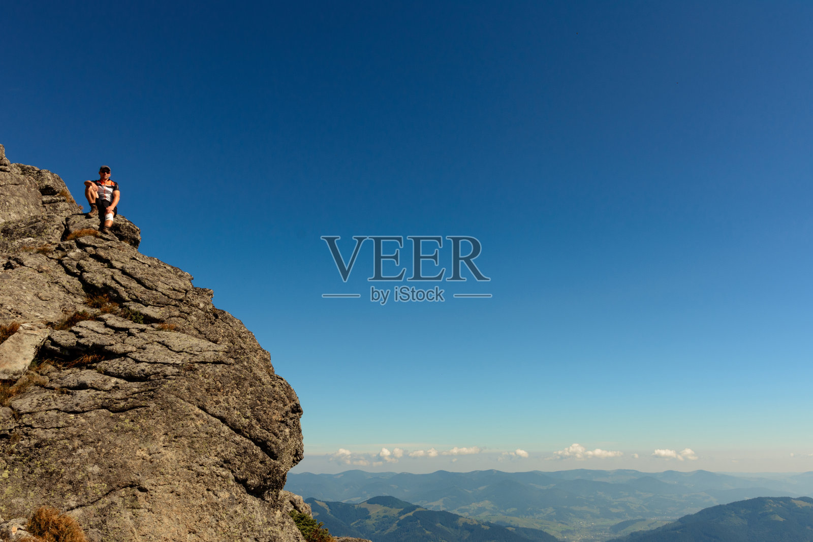 一个男人站在乌克兰喀尔巴阡山脉山峰的一块石头边上，黑山山脊是喀尔巴阡山脉被践踏的小径上风景如画的山脉。照片摄影图片