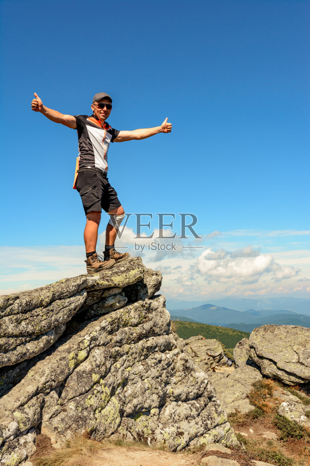 一个男人站在乌克兰喀尔巴阡山脉山峰的一块石头边上，黑山山脊是喀尔巴阡山脉被践踏的小径上风景如画的山脉。照片摄影图片
