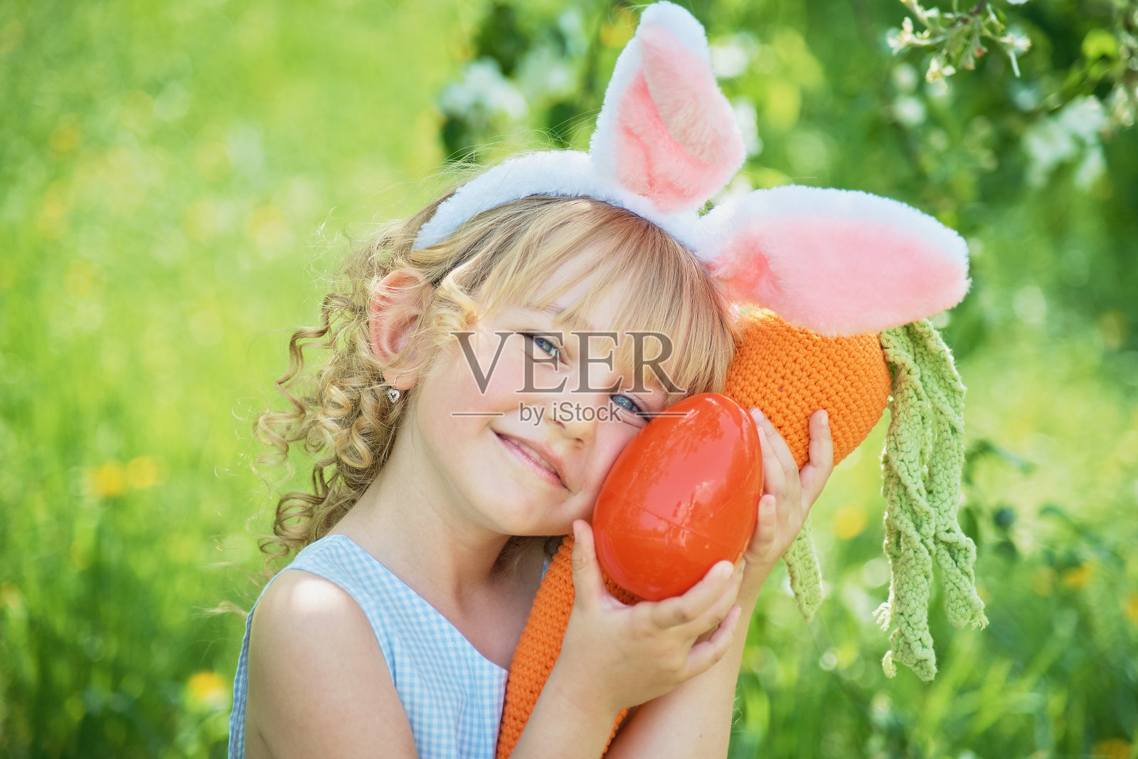 可爱有趣的女孩在花园里拿着复活节彩蛋和兔子耳朵。复活节的概念。寻找复活节彩蛋时笑着的孩子照片摄影图片