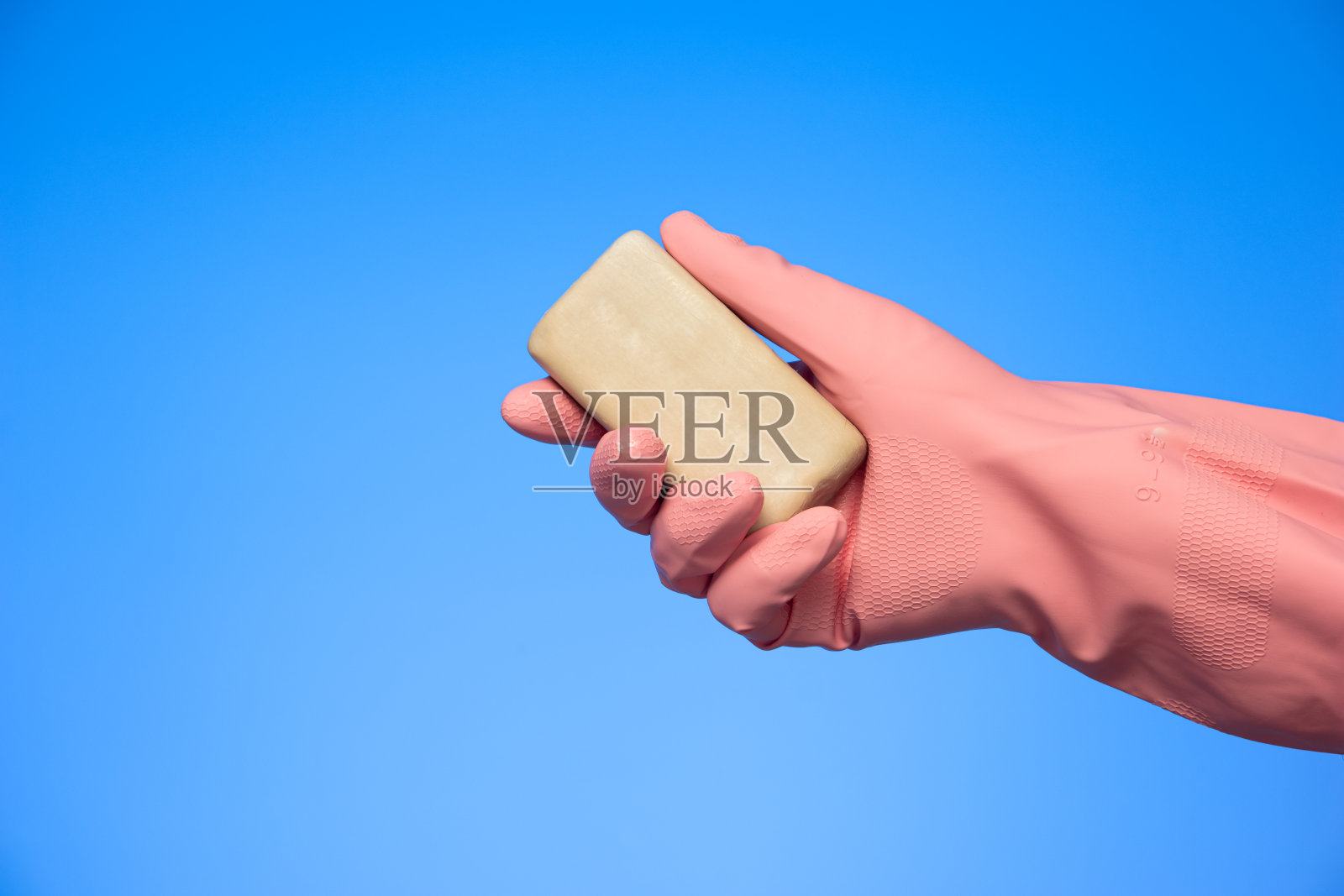 白种人手持肥皂条，戴着乳胶清洁手套，在蓝色背景的摄影棚里拍摄照片摄影图片