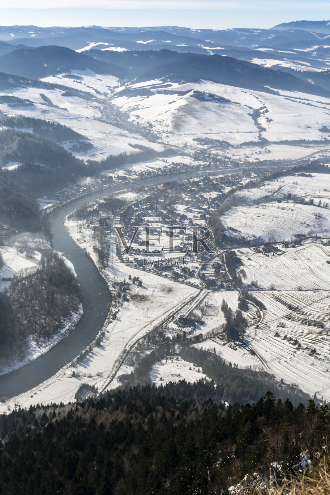 这是冬季风景中的一个村庄，位于波兰松树山的一条河边，从上面俯瞰。照片摄影图片