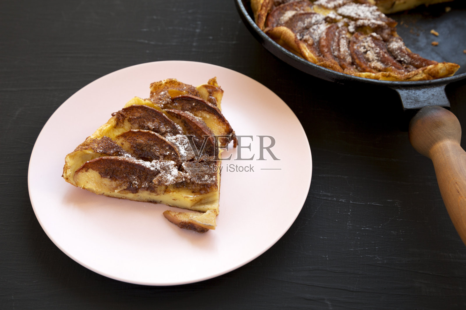 自制的苹果荷兰薄饼放在一个粉红色的盘子上，黑色的背景，侧视图。照片摄影图片