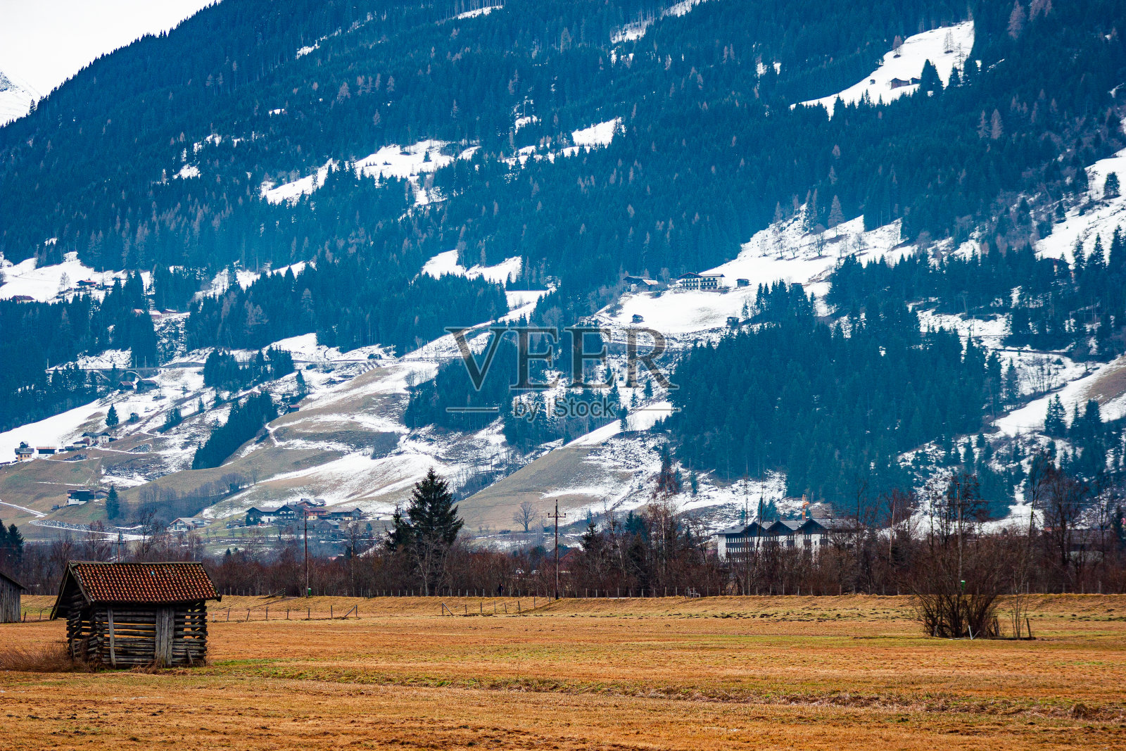 木头覆盖的仓库结构，用于储存干草和木柴，在野外前景，一个巨大的山可以看到在背景，酒店和建筑在远处照片摄影图片