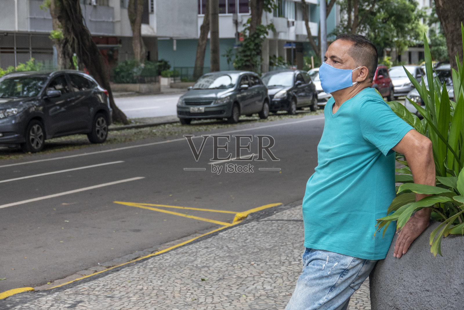 戴着面具的男人倚靠在一棵树上望着街道照片摄影图片