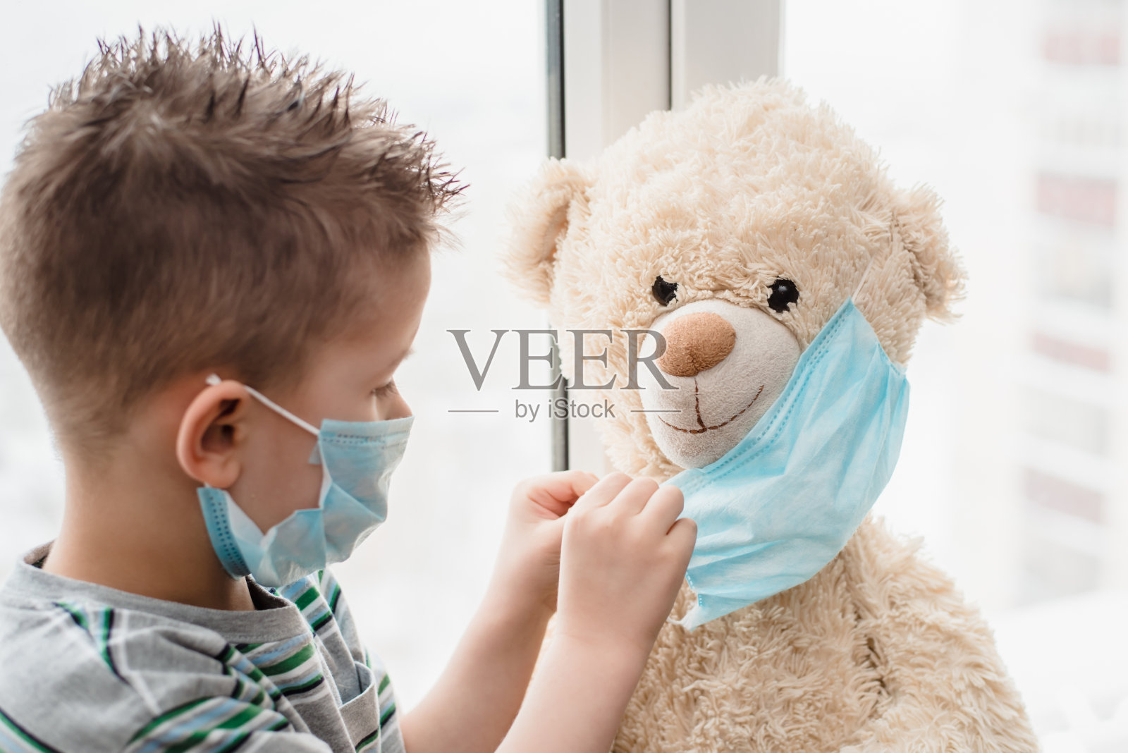 一个被隔离的小孩在家里帮助一只泰迪熊戴上医用口罩。预防冠状病毒和冠状病毒- 19。概念照片摄影图片