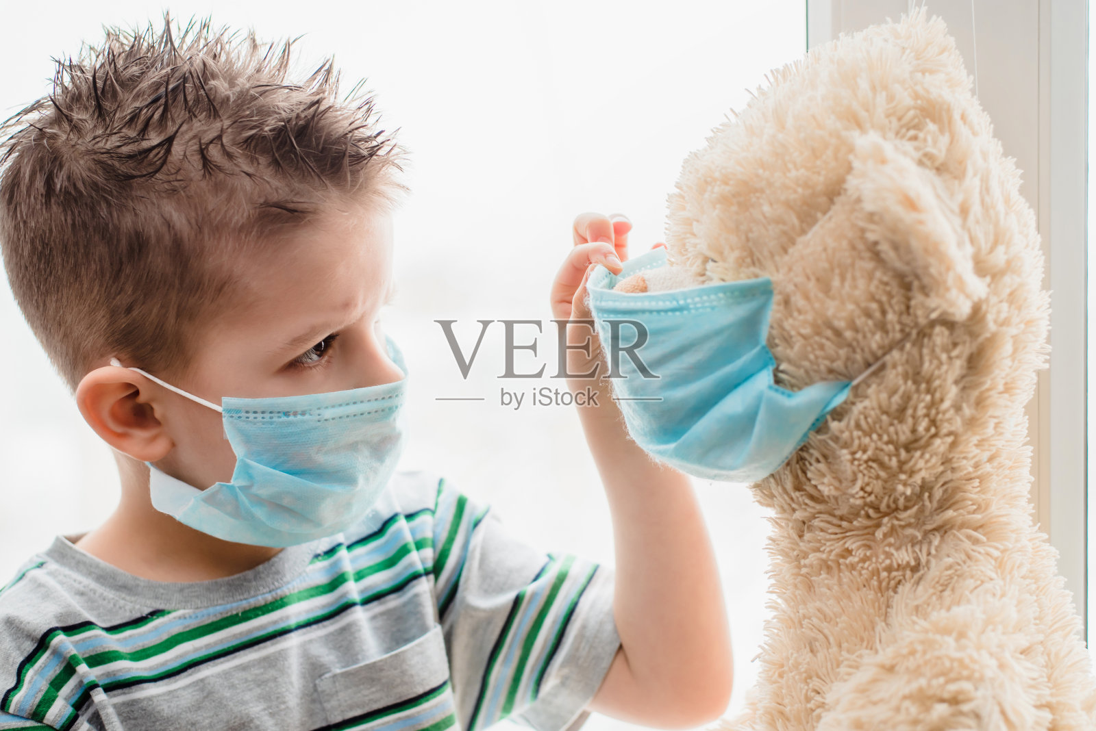 一个被隔离的小孩在家里帮助一只泰迪熊戴上医用口罩。预防冠状病毒和冠状病毒- 19。概念照片摄影图片