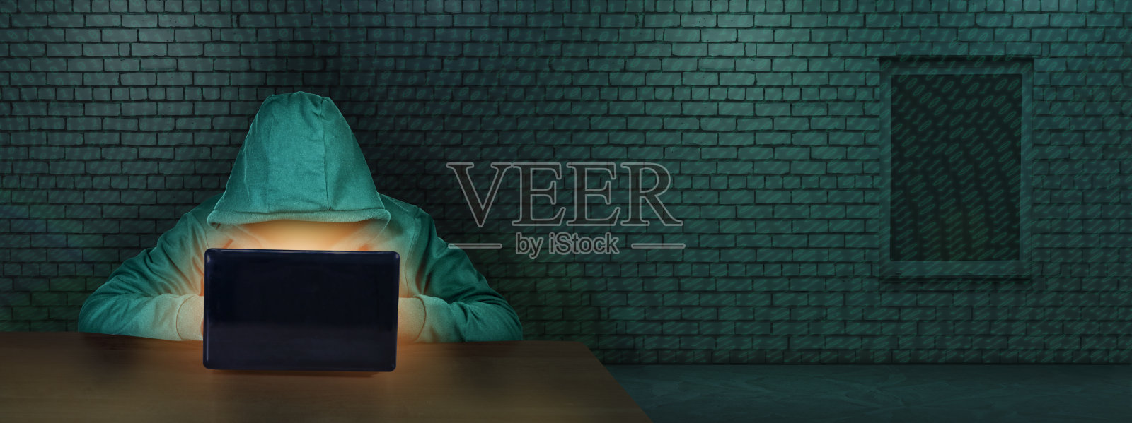 黑客在一间有砖墙的房间里，在笔记本电脑屏幕后面工作。网络犯罪。黑客和恶意软件的概念，网络安全。数字的罪行。照片摄影图片