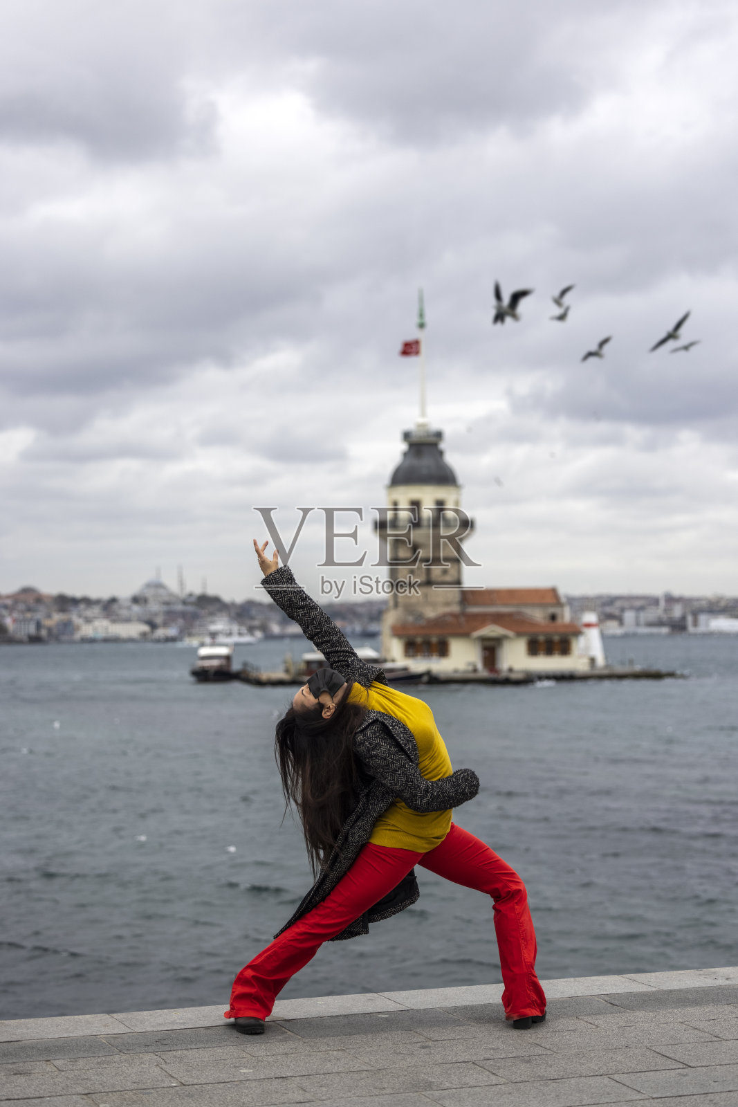 在伊斯坦布尔市的少女塔前，拿着红色的雨伞跳舞照片摄影图片