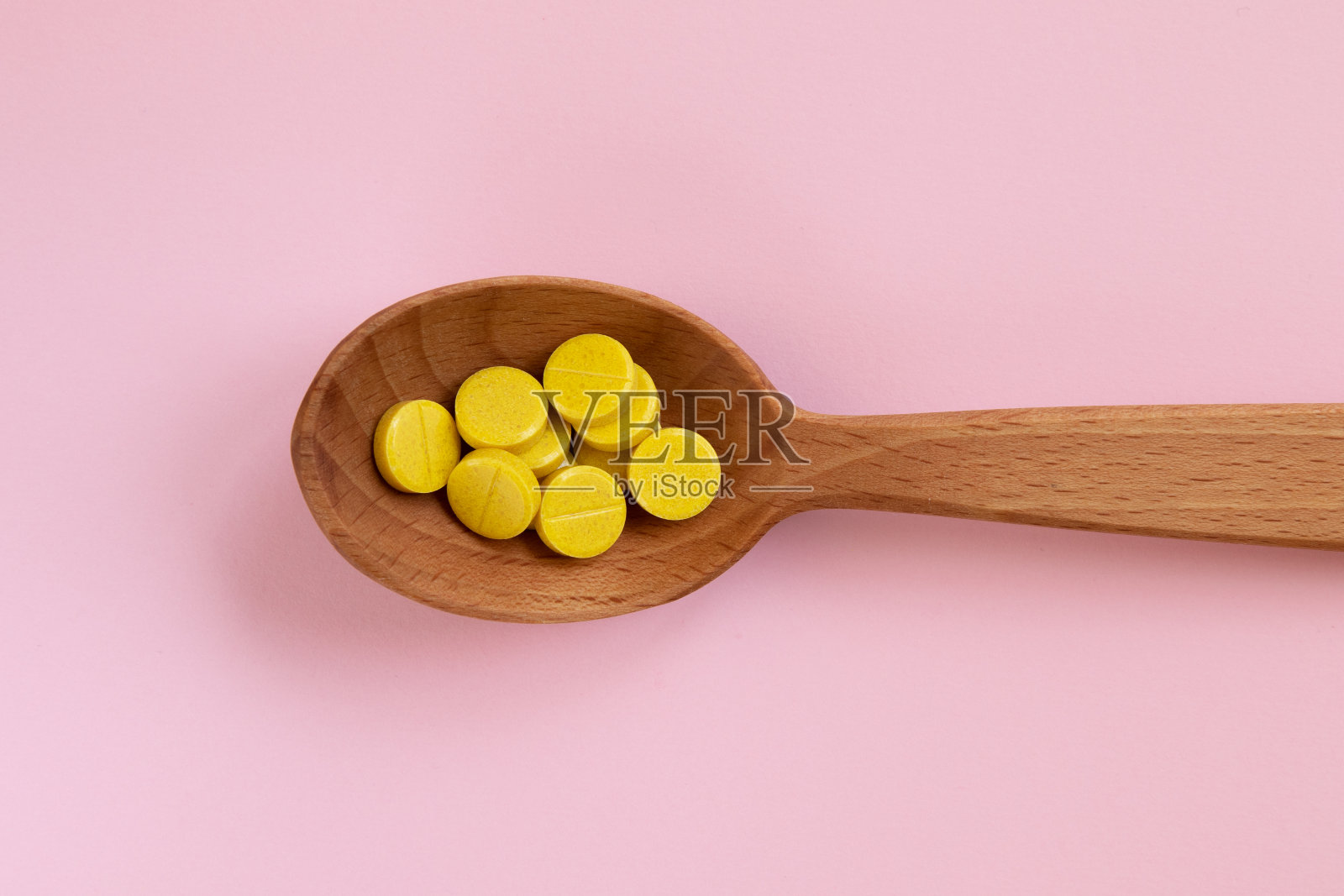 黄色药丸，装在木勺里，粉色背景。医学健康理念。照片摄影图片