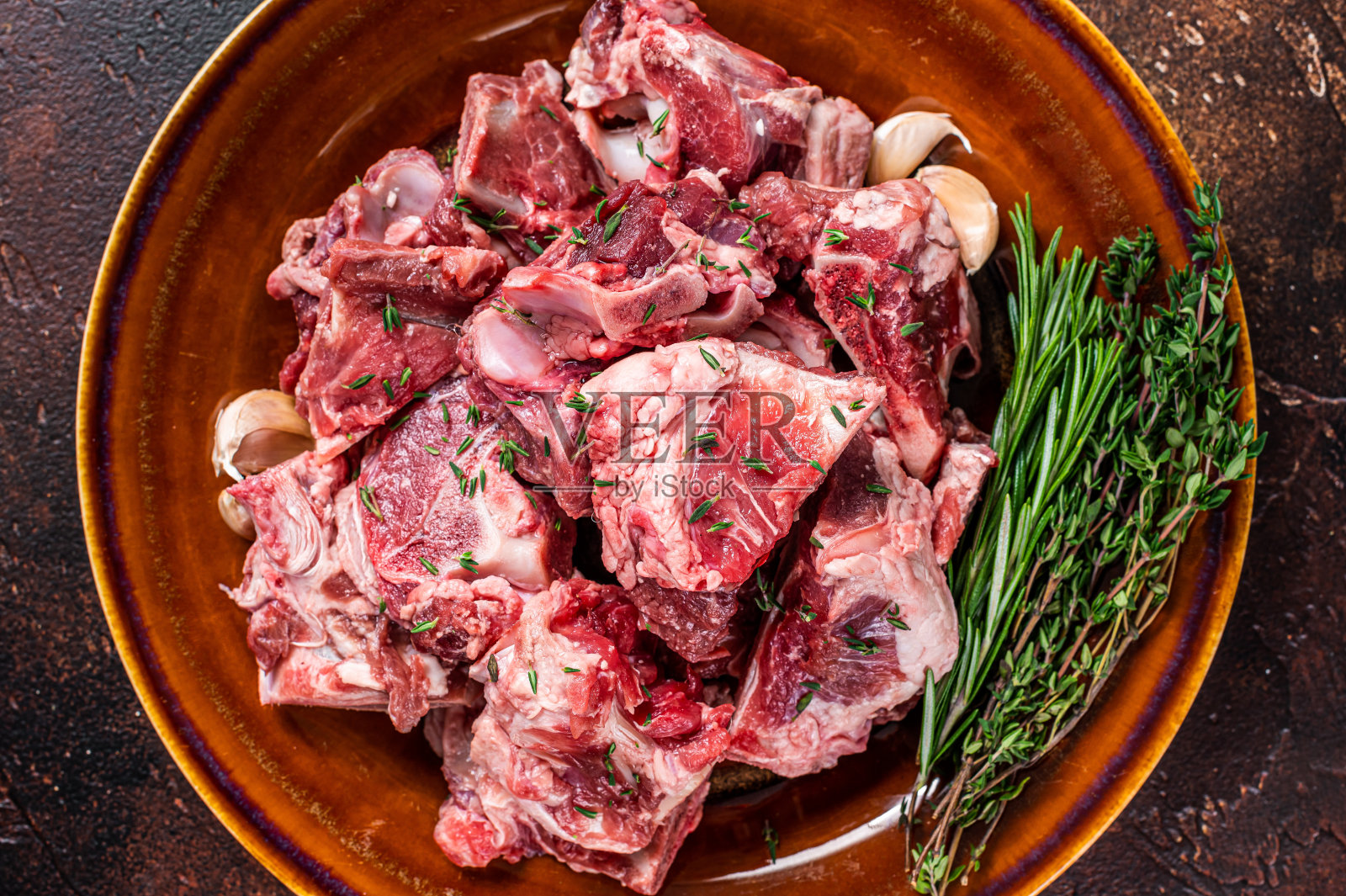 切成小块的生羊肉，用于炖牛肉或与骨头一起炖在质朴的盘子上。黑暗的背景。俯视图照片摄影图片