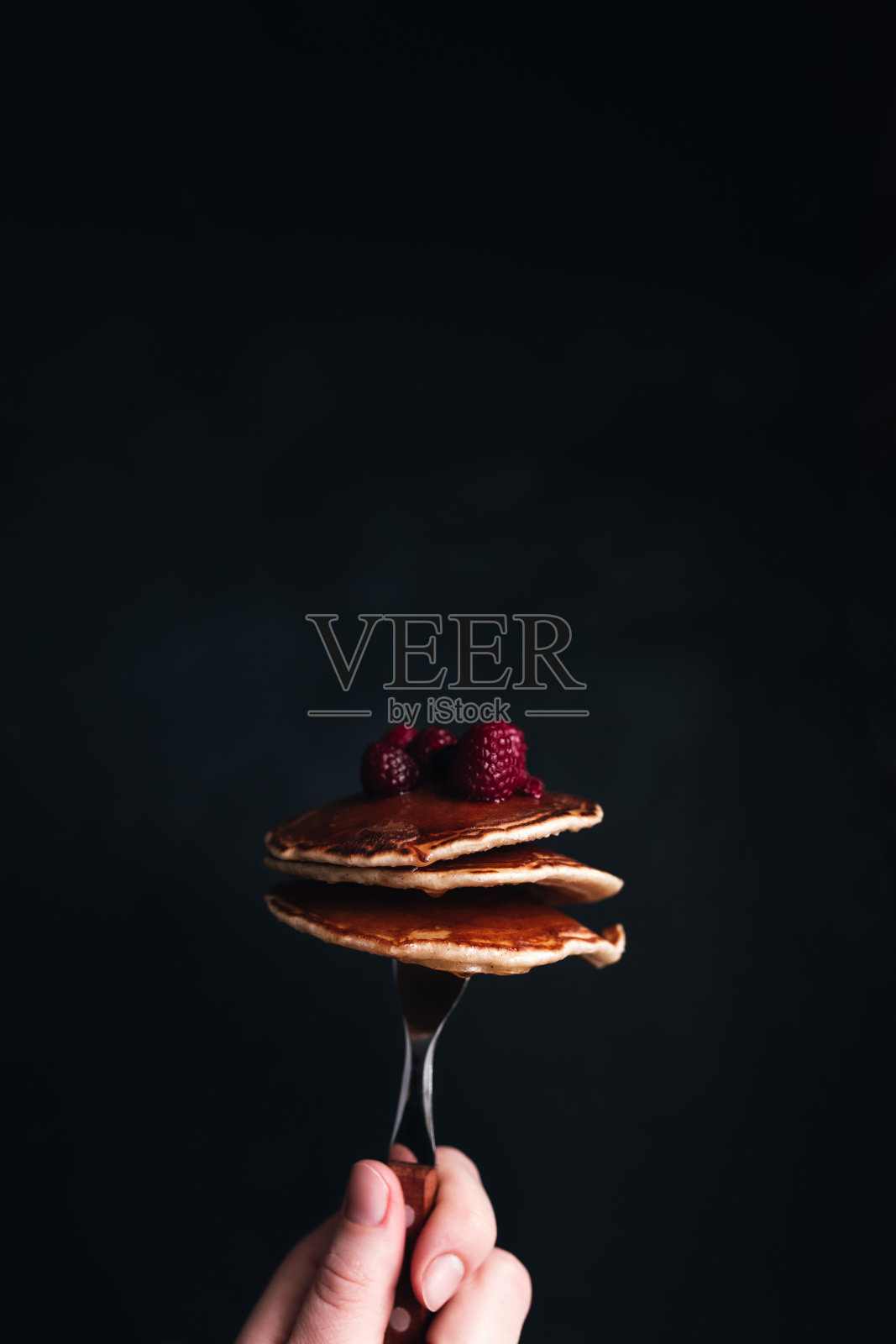 手里拿着一把叉子，叉子上放着多汁的煎饼，还有浆果和蜂蜜照片摄影图片