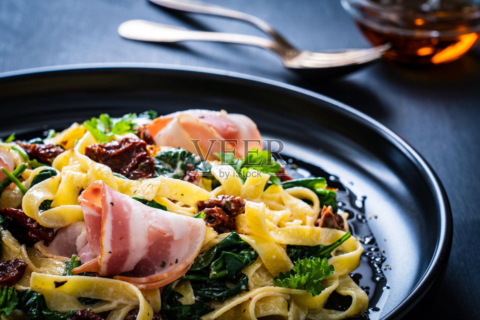 黑色的桌子上放着菠菜，培根，晒干的番茄和阿尔弗雷多酱照片摄影图片