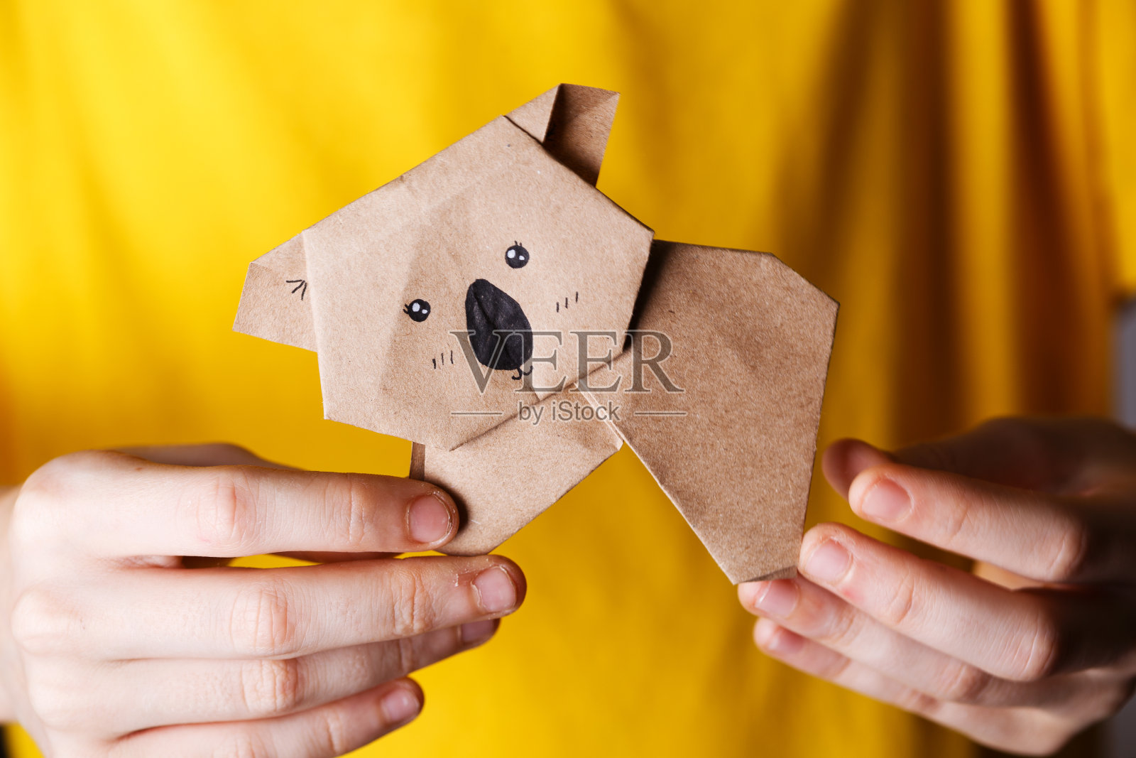 在黄色背景上，女孩手里拿着一只折纸树袋熊。有趣的爱好“n照片摄影图片