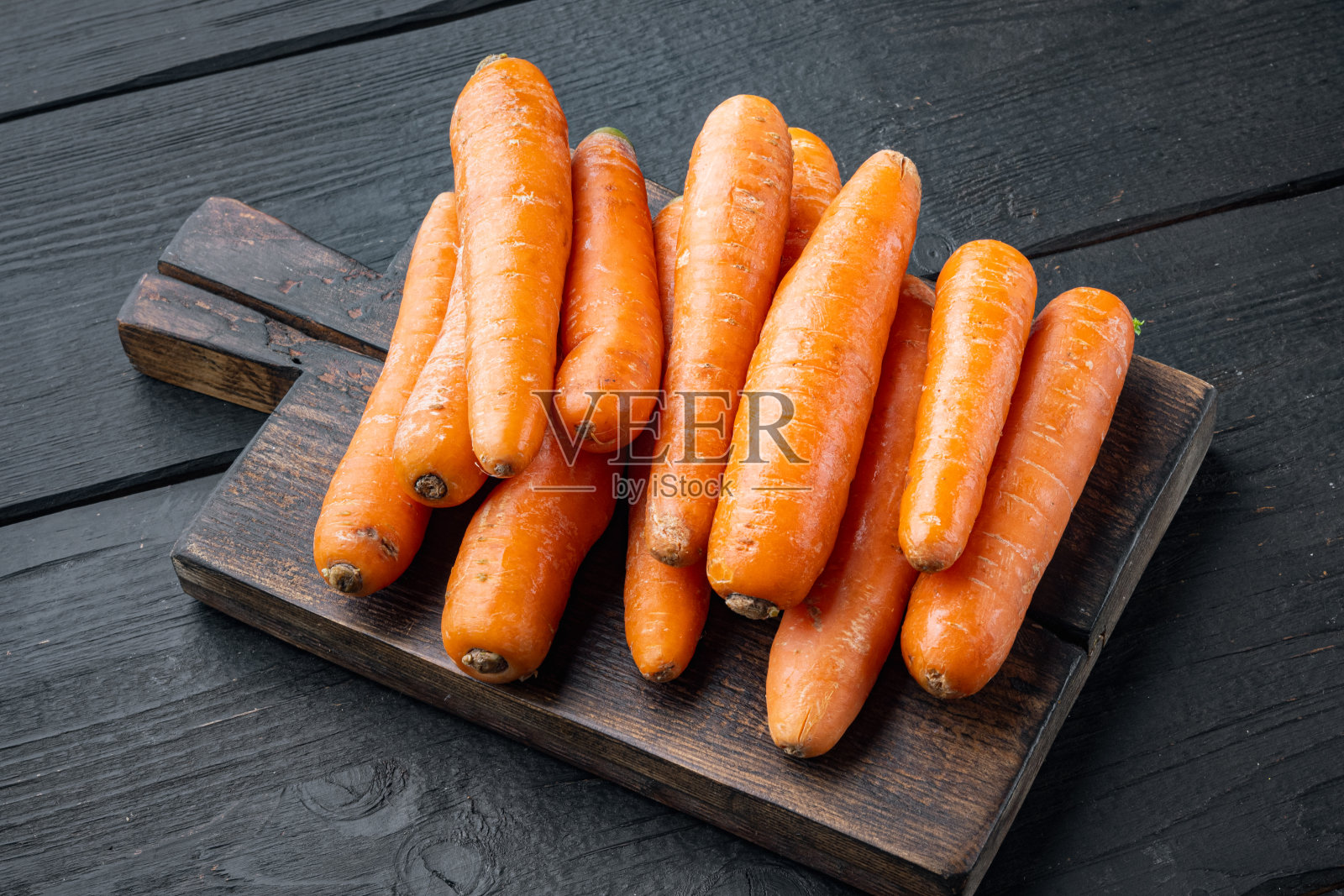 一束束彩色的橙色胡萝卜，放在木砧板上，黑色的木桌背景上照片摄影图片