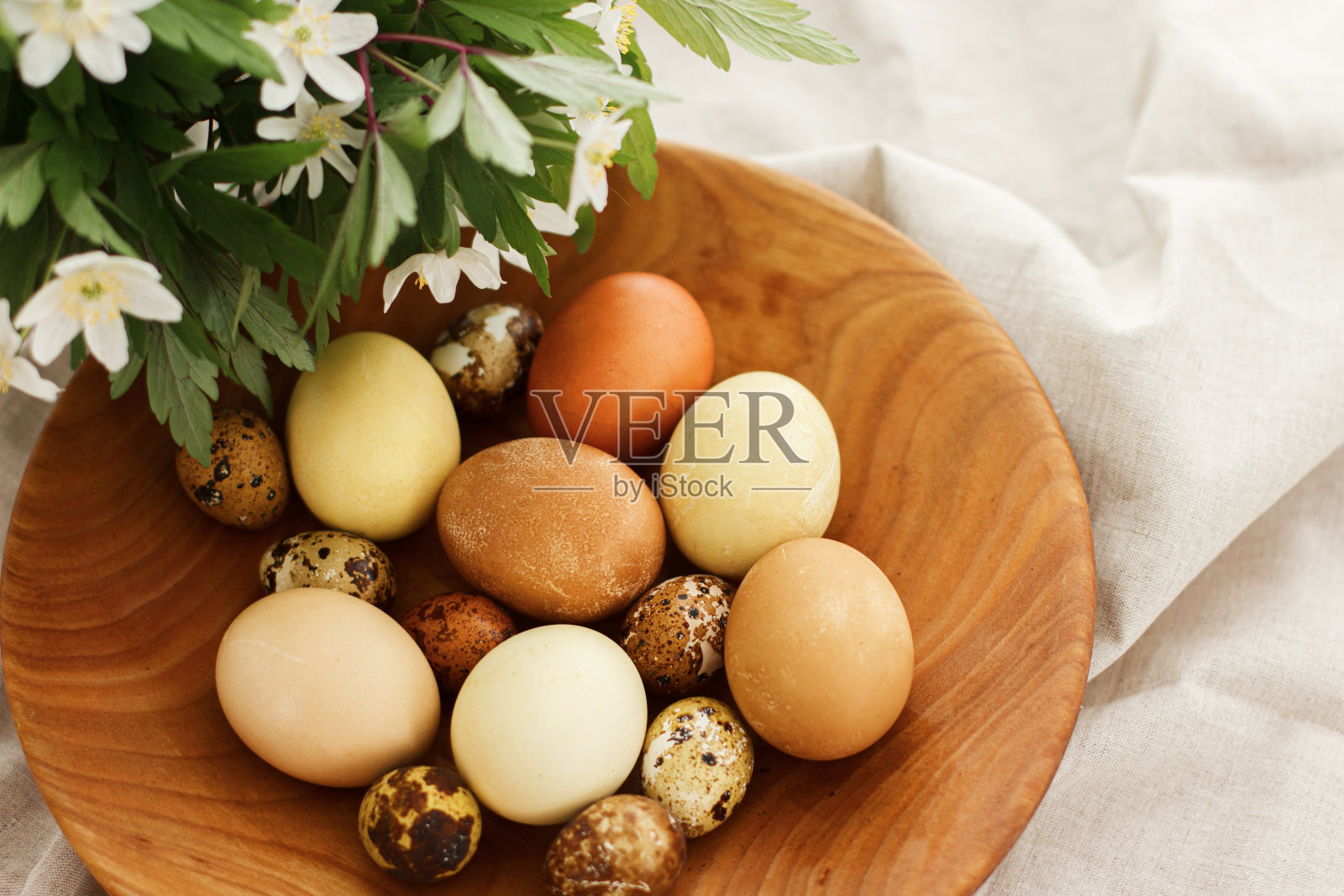 复活节快乐!现代的复活节彩蛋装在木碗里，朴素的亚麻布和春天的花朵。审美照片摄影图片