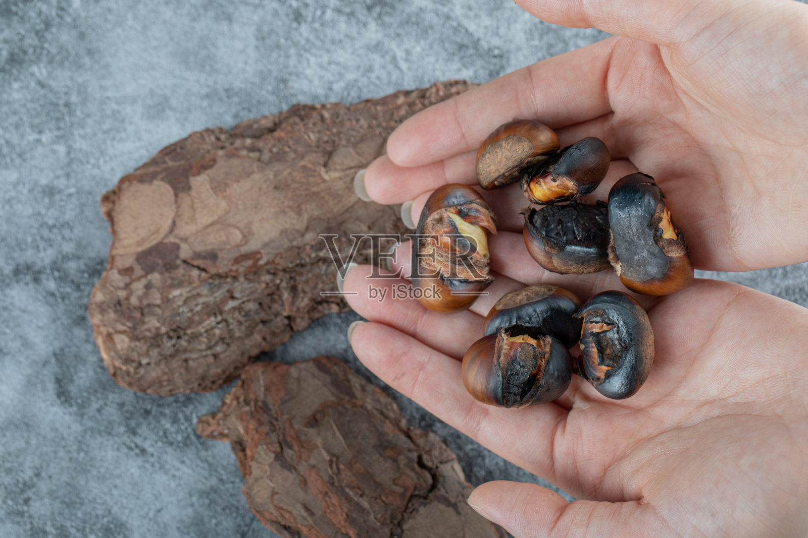 灰色背景下，双手握着炸栗子照片摄影图片
