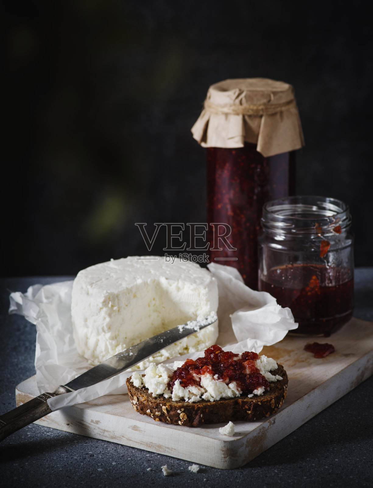 深色背景的切菜板上，夹着白软干酪和果酱的三明治。照片摄影图片