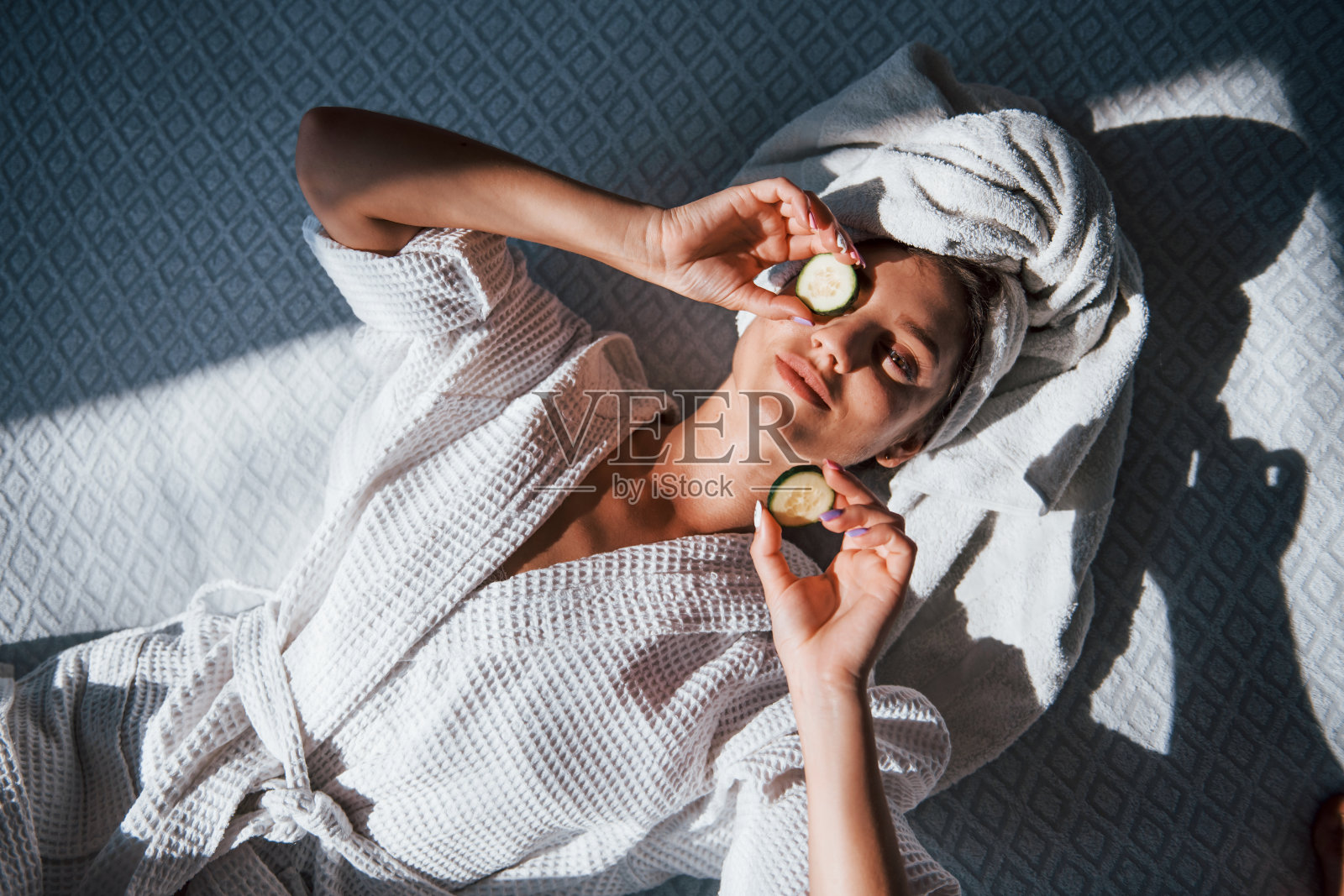 年轻的积极妇女用毛巾在头上和黄瓜躺在床上照片摄影图片