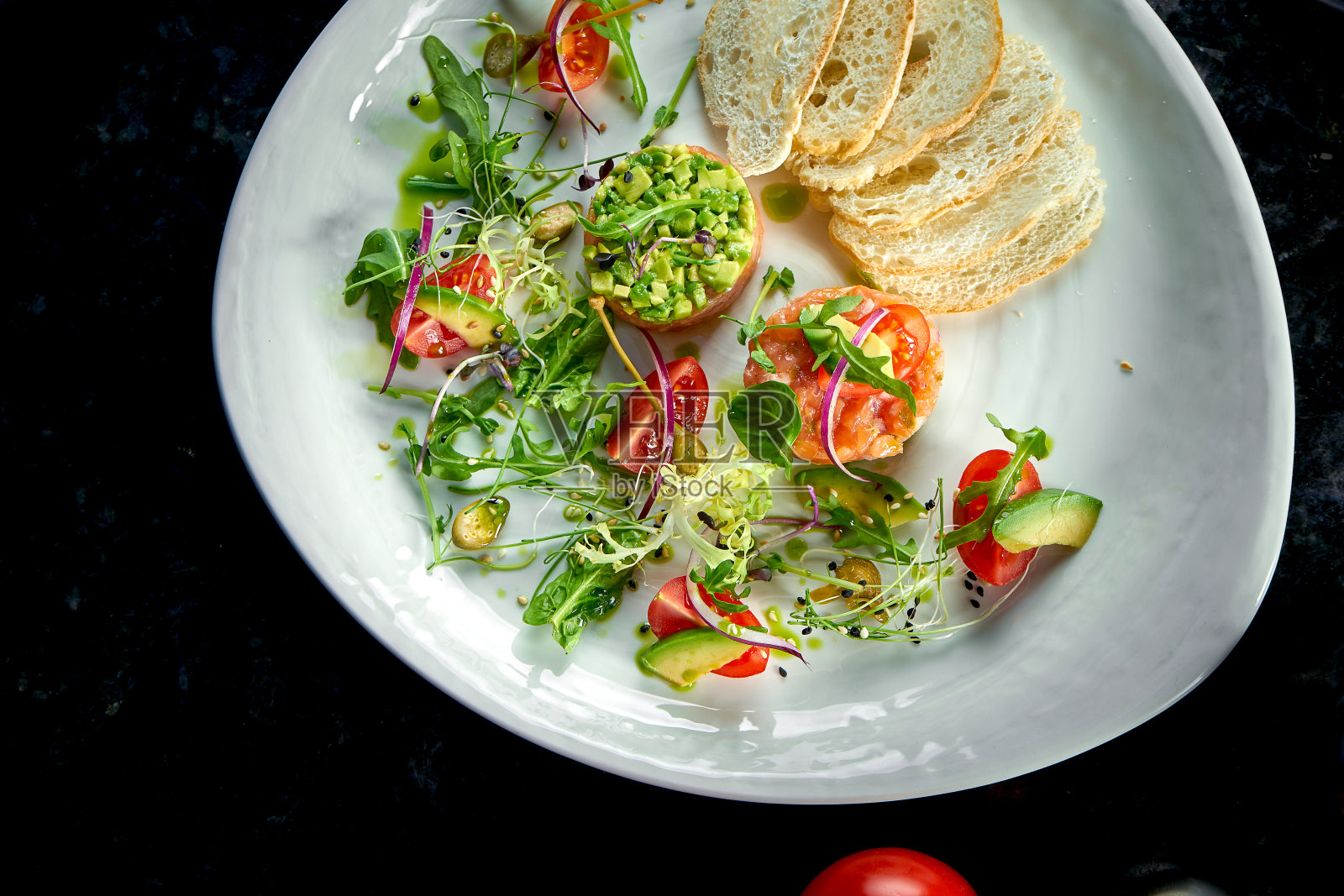 主菜前的法式开胃菜——三文鱼排鞑靼配鳄梨、樱桃番茄和油炸面包丁，盛在一个白色盘子里。餐厅的食物。从上面的观点照片摄影图片