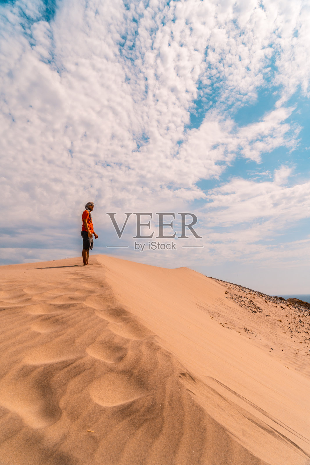 一名身穿红色衬衫、头戴头巾的男子，正在安达卢西亚尼贾尔加塔Cabo de Gata自然公园里的Playa de Mónsul沙丘沙漠中行走。西班牙、地中海照片摄影图片