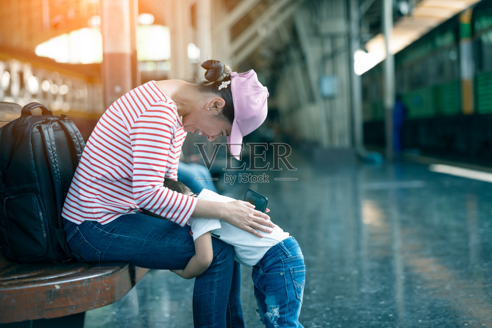 在站台上等车的时候，年轻的妈妈逗着她的小孩玩。两人都很开心，一起笑。照片摄影图片