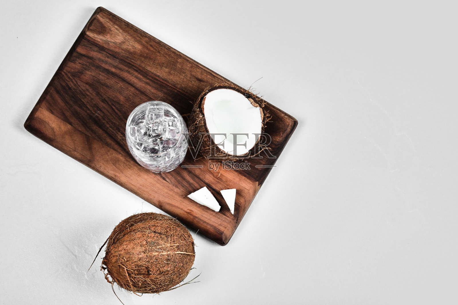 在木板上切一半的椰子和一杯加冰的水照片摄影图片