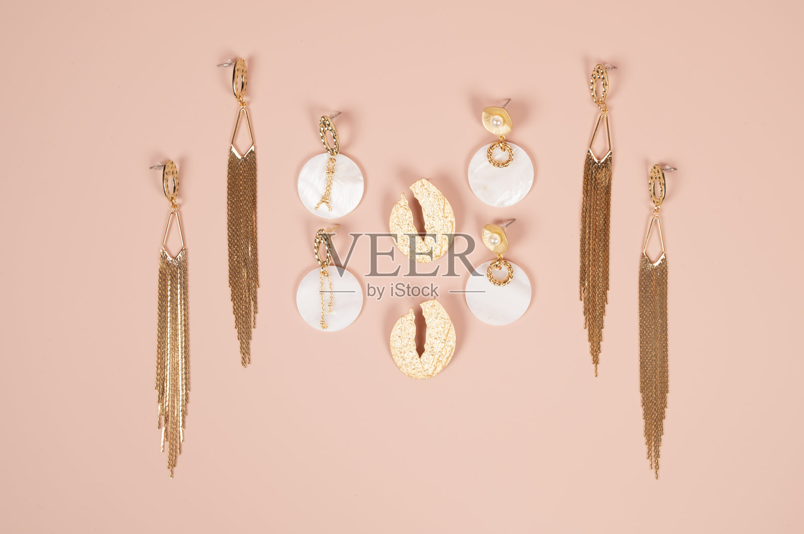 顶视图美丽的豪华金耳环在粉红色的表面。女士时尚时尚的配饰安排。时尚珠宝。照片摄影图片