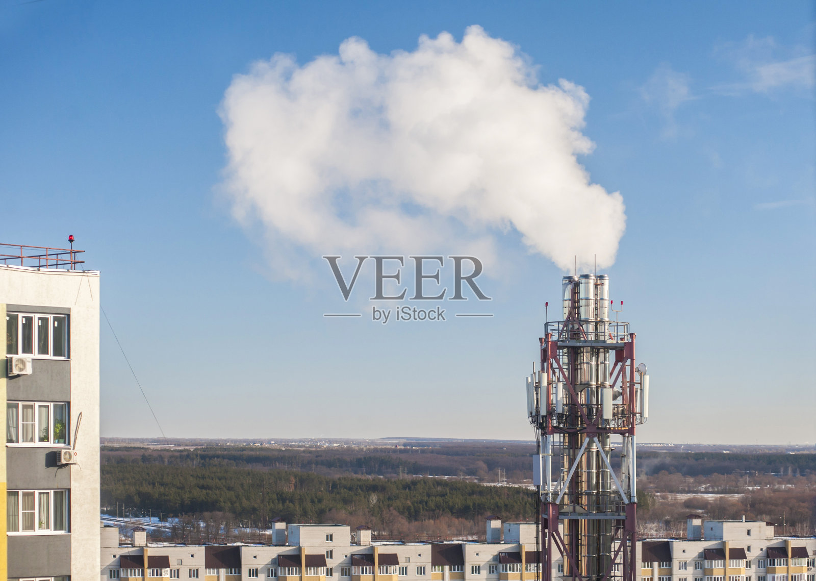 锅炉房的烟囱映衬着蓝天。在住宅楼的背景下，蒸汽从管道中冒出。特写镜头照片摄影图片