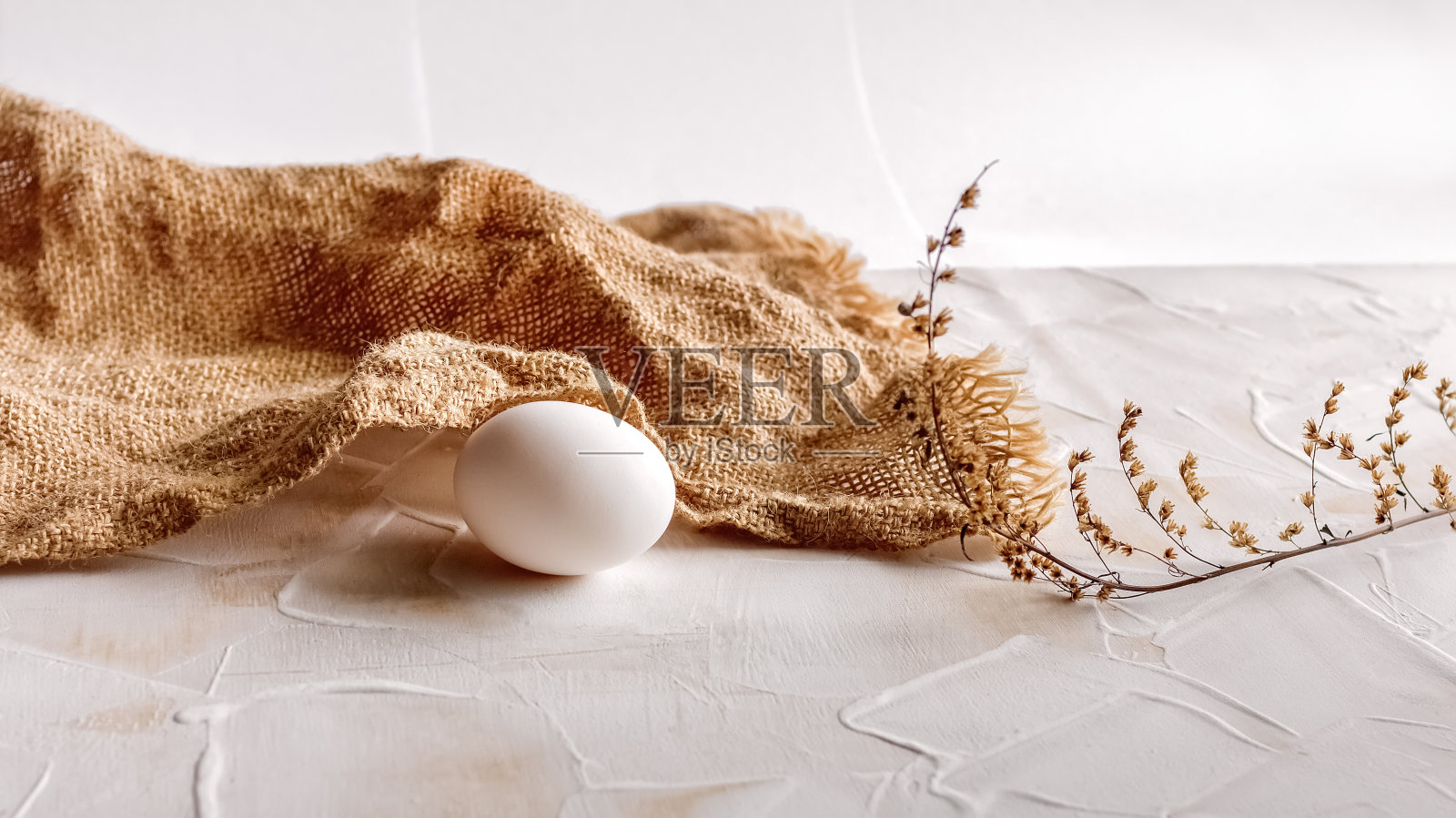 一个白色的鸡蛋，粗麻布和一根干草在一个孤立的光背景。自然与健康营养的概念。照片摄影图片