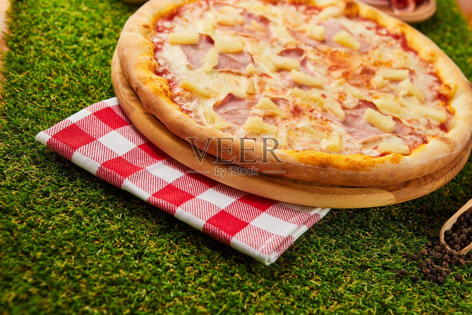 传统的意大利披萨，火腿，马苏里拉奶酪和菠萝在绿色草地的背景照片摄影图片