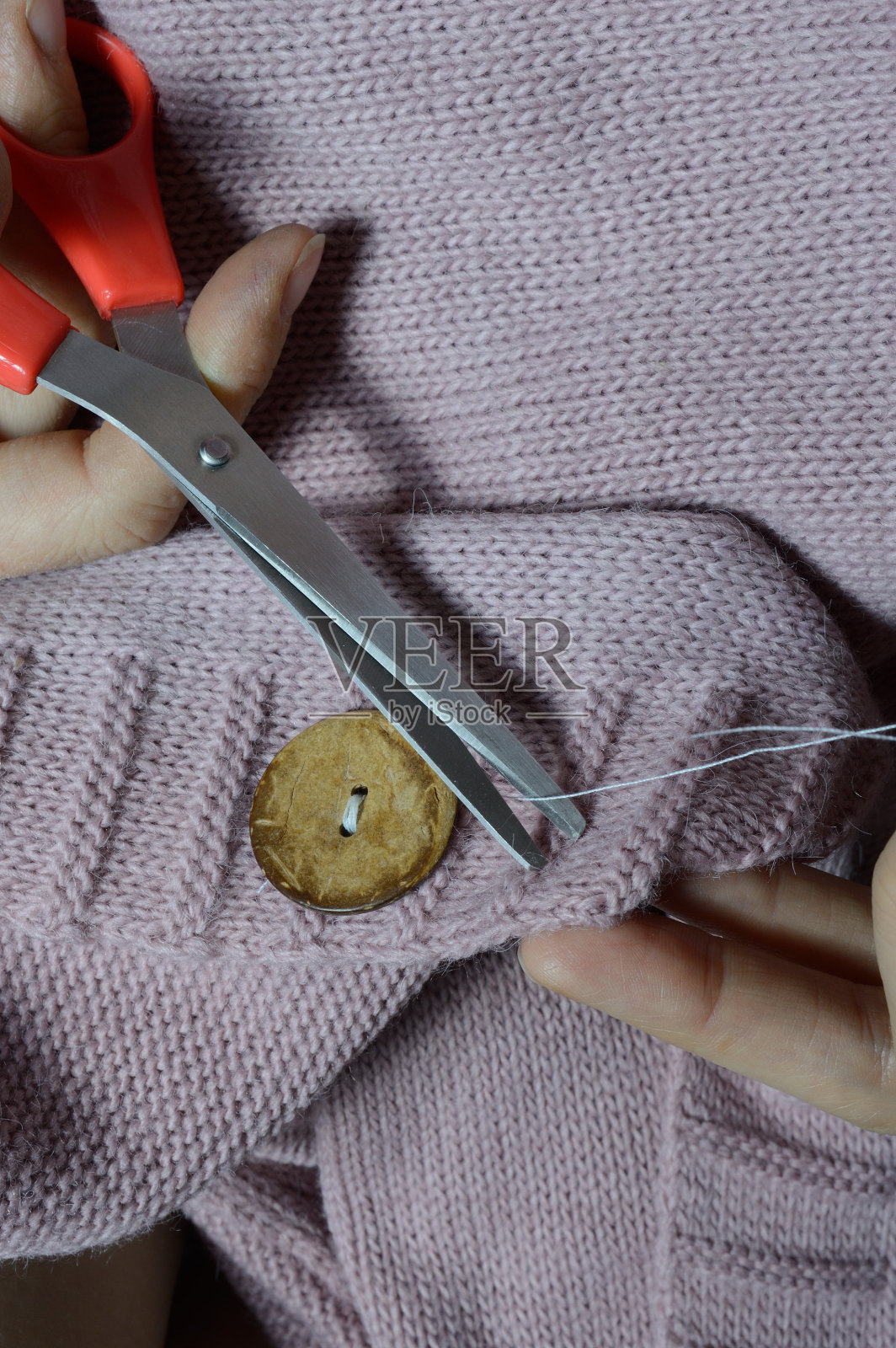 女工们用手在夹克上缝上一颗木扣子。特写镜头。照片摄影图片