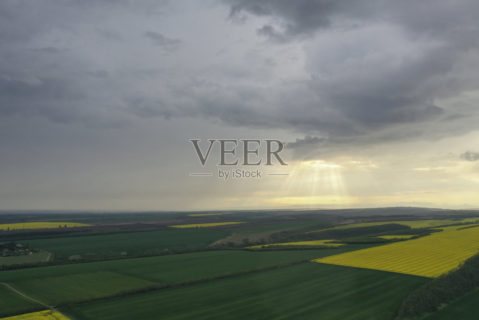 黄花油菜田和麦田阴天多云坏天气。太阳从乌云中照射出来。无人机鸟瞰图。为石油工业提供绿色植物能源。欧洲匈牙利照片摄影图片