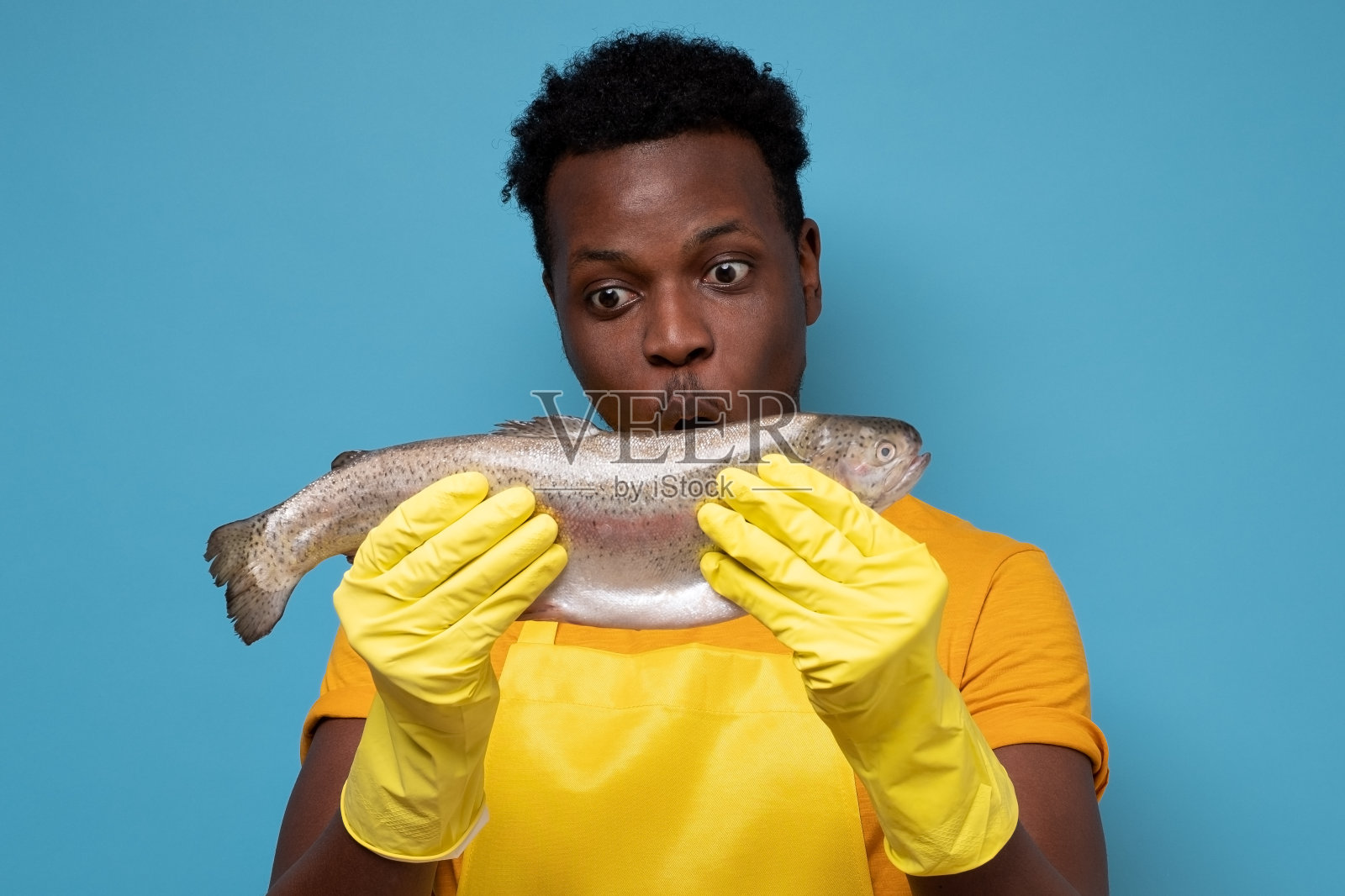 高兴的渔夫穿着黄色的t恤，手套和围裙看着鱼。照片摄影图片