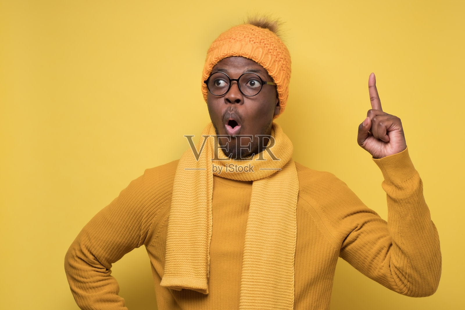 非洲男子戴着温暖的围巾和帽子，向上伸出食指，有主意。照片摄影图片