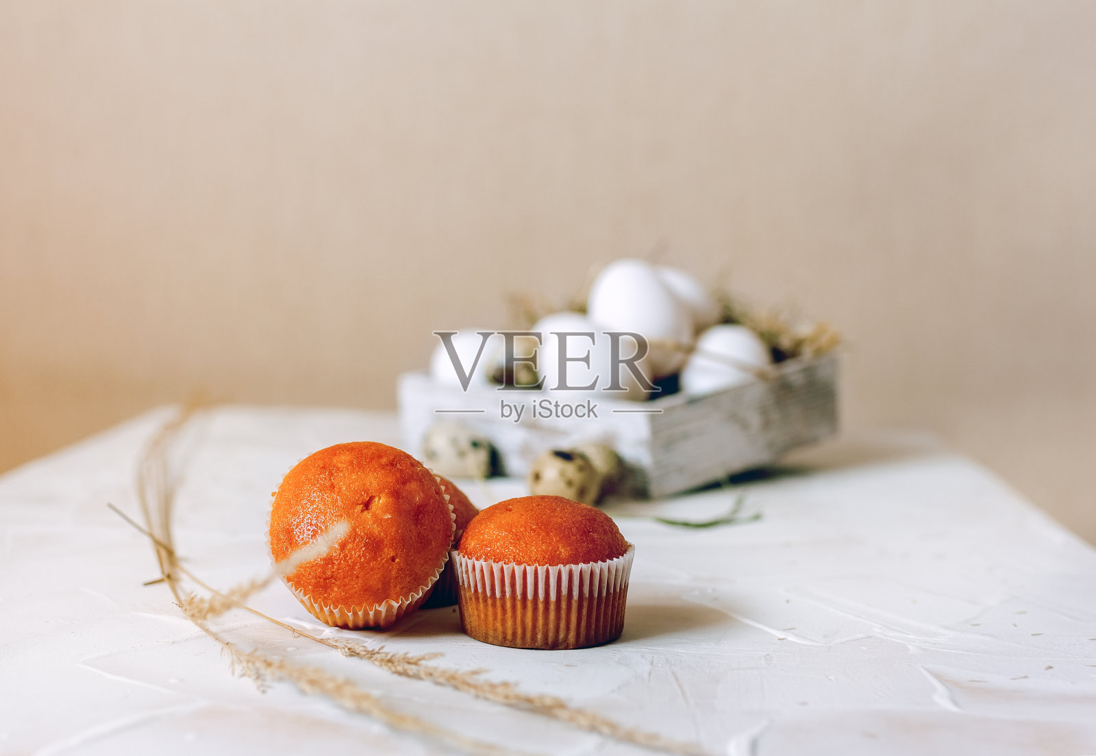 复活节的背景。纸杯蛋糕放在明亮的桌面上。一盒白色的鸡蛋模糊地站在背景上。照片摄影图片