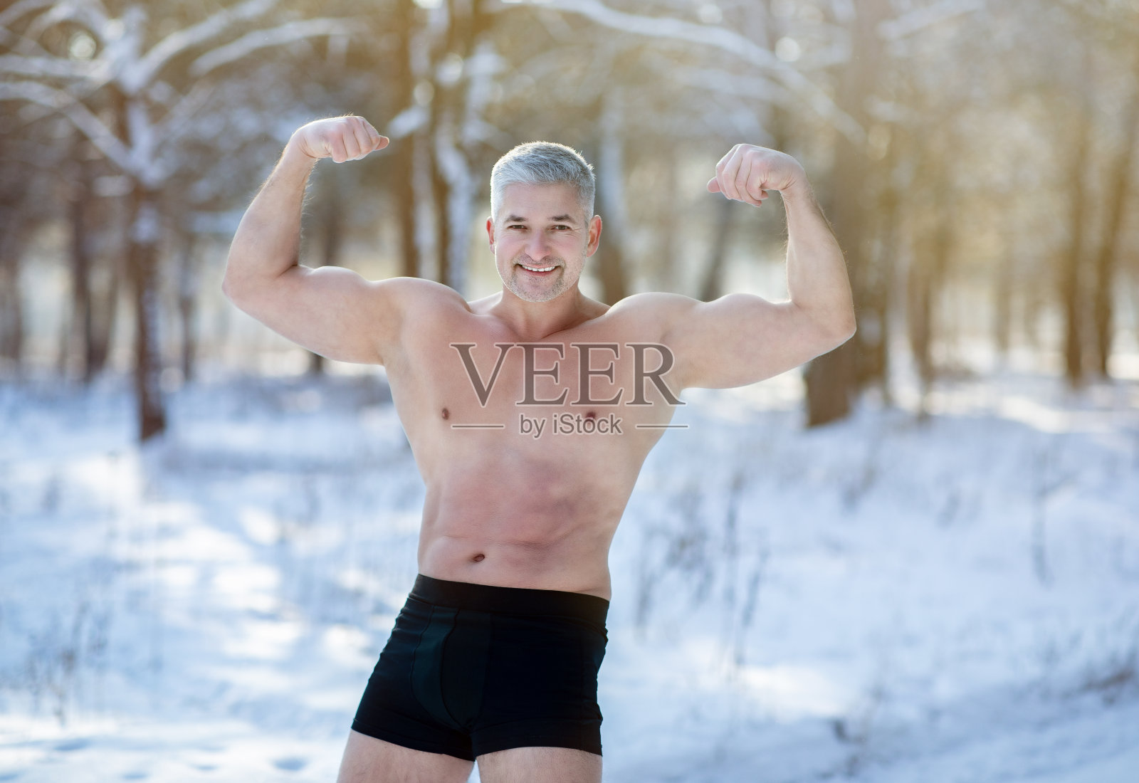 英俊的老男人赤裸的躯干显示他强壮的二头肌在冬天霜冻在雪林。适应环境的概念照片摄影图片