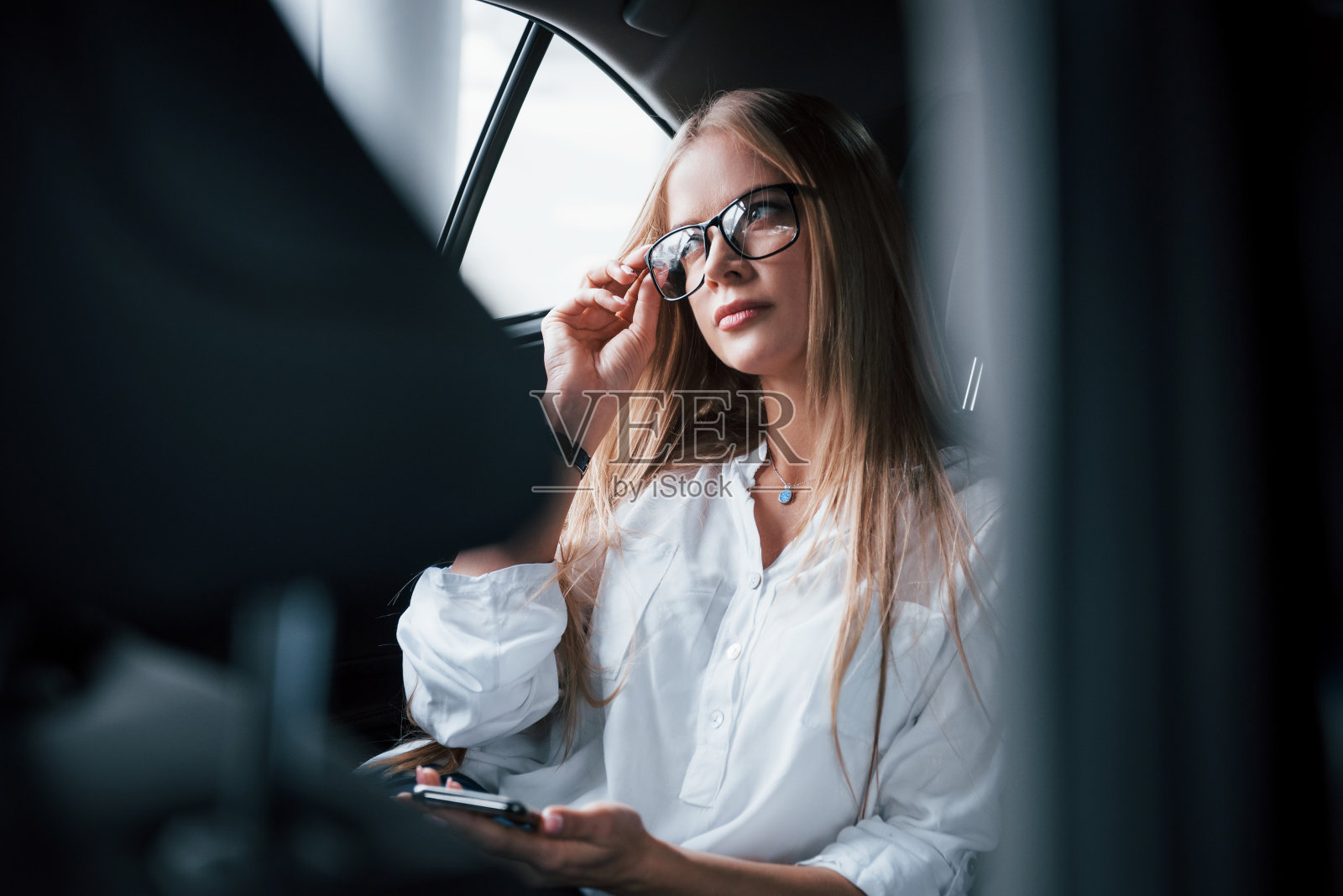 在等司机的时候放松。聪明的女商人坐在黑色内饰豪华轿车的后座上照片摄影图片
