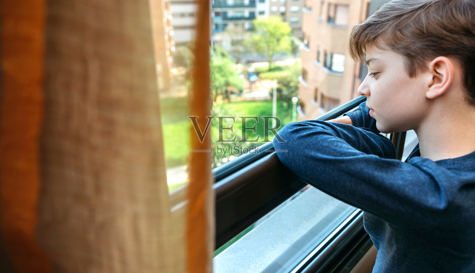 被冠状病毒封锁的男孩透过窗户看照片摄影图片